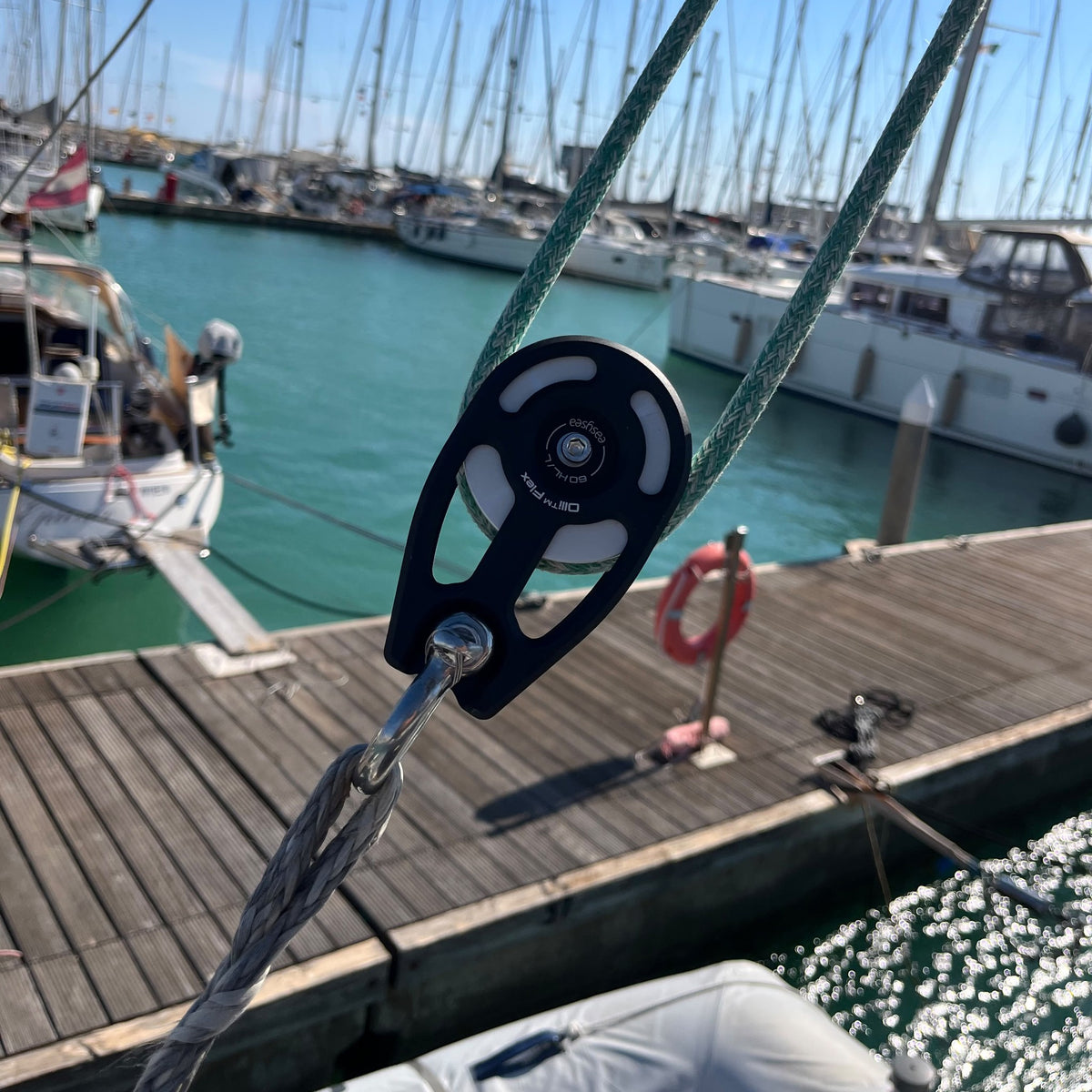 Olli Flex HL black modular block in use on a sailboat, green sheet running through, marina in the background